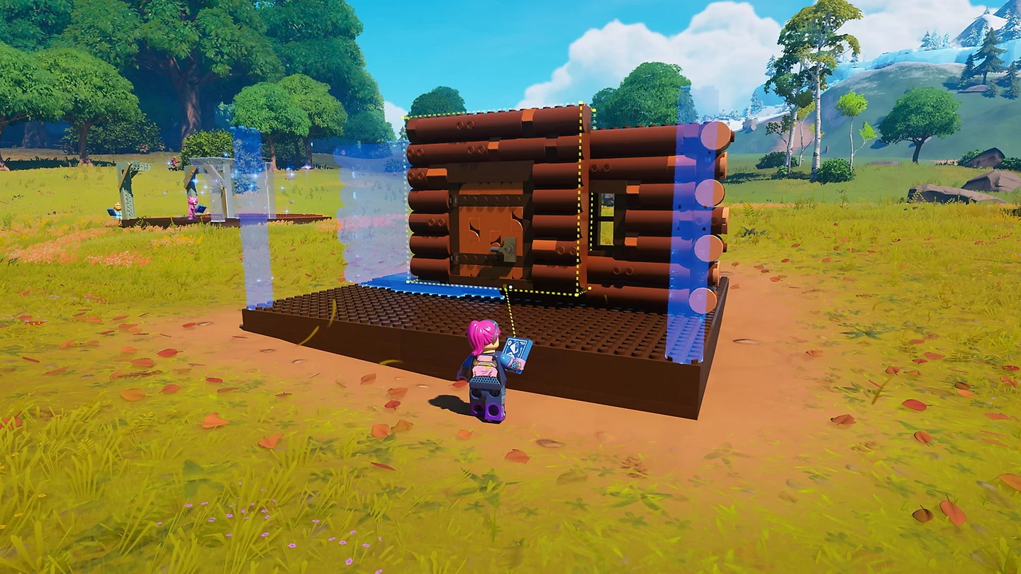 Minifigura de cabelo rosa monta uma cabana de troncos peça por peça sobre uma base de LEGO, no meio de um campo gramado